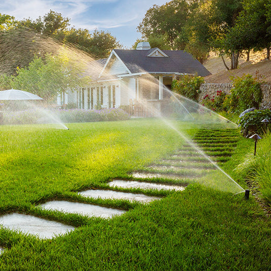 Sprinkler system watering a grassy lawn with a house in the background