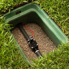 Green plastic container with a black pipe and red valve on a grassy background