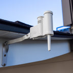 White outdoor sensor or device mounted on a building exterior with blue sky background