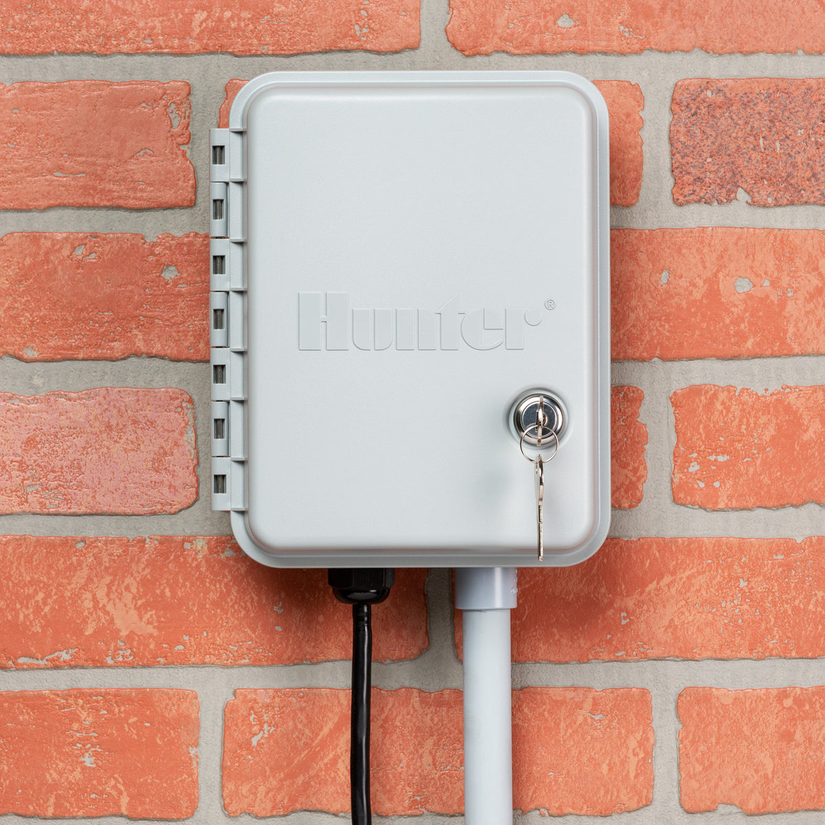 Gray Hunter X-Core irrigation controller with lock and key mounted on brick wall.