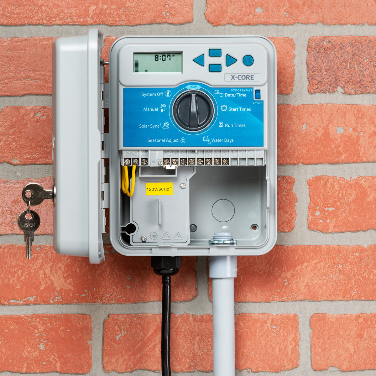 Hunter X-Core irrigation controller with blue dial interface and open gray plastic casing mounted on brick wall.